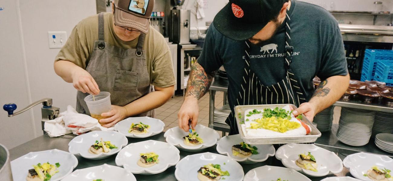 Chef Alan Sternberg and assistants prepare dishes on the line. Ceramics by Tim Compton; wheel-thrown, Cone 6 porcelain, 8x8x3 in. each. Photograph by Audra Sternberg, 2017.